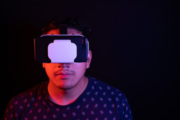 Young latin man using Virtual Reality VR Headset 3D Glasses. Dark backdrop. Low key. Copy space.