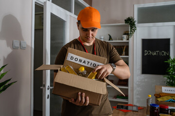 One man caucasian volunteer working at charity foundation preparing box with food for donation...