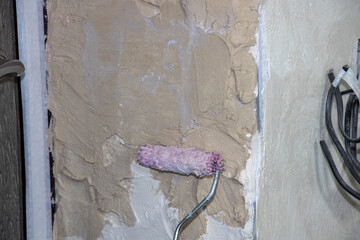 Preparing the wall for leveling with plaster. Priming a concrete wall with a roller.