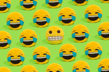 Scheme of yellow smiley pillows laughing at a smiley with a embarrassed grimace on a green background. - obrazy, fototapety, plakaty