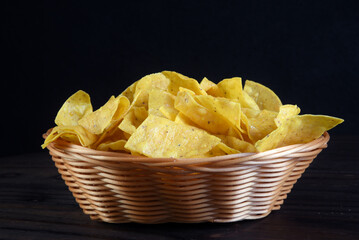 portion of corn nachos, mexican chips in reed bowl isolated on black background