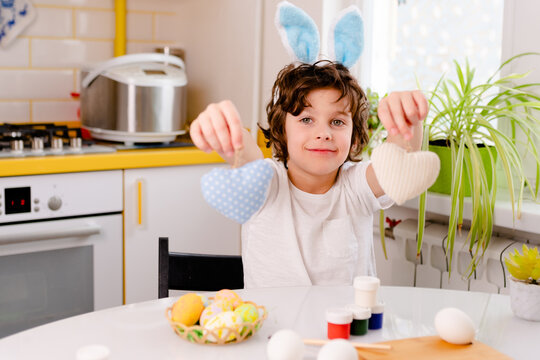 dyeing Easter eggs. curly boy dressed in white Tshirt and blue bunny ears paints Easter eggs.