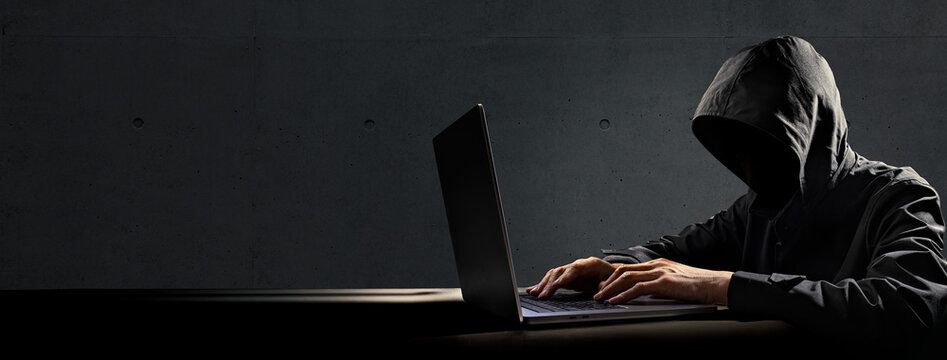 ノートパソコンを操作しているハッカー、犯罪者のイメージ