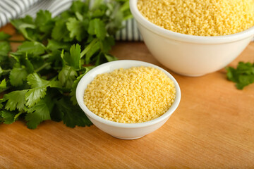 Bowls of raw couscous with parsley on table