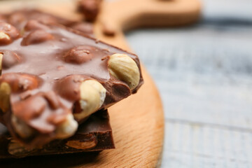 Pieces of tasty chocolate with hazelnuts on board, closeup