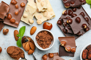 Pieces of tasty chocolate with nuts and cacao powder on color background