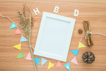 Flat lay of blank photo frame with HBD happy birthday wooden alphabet mockup on wooden table background.