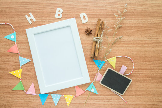 Flat lay of blank white photo frame with happy birthday wooden alphabet mockup on wooden table background. Lifestyle and design decor concept.