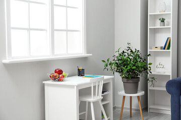 Modern workplace with stationery and fruit basket in light room