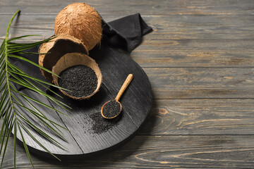 Coconut shells and spoon with activated carbon on wooden background - obrazy, fototapety, plakaty