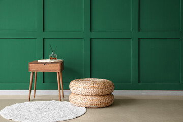 Wooden table with reed diffuser and rattan poufs near green wall
