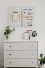 Fototapeta na wymiar Chest of drawers with frames and pegboard hanging on light wall