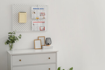 Chest of drawers with frames and pegboard hanging on light wall