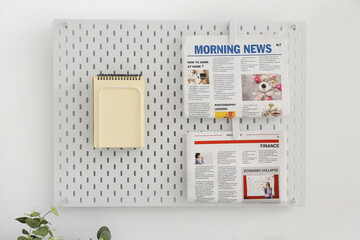 Pegboard with notebooks and newspapers hanging on light wall