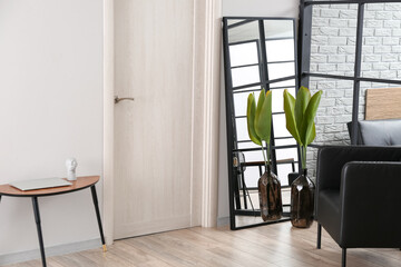 Interior of stylish room with armchair and mirror near light door
