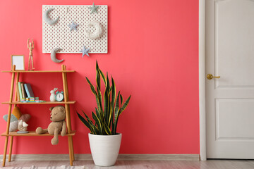Shelving unit with toys, houseplant and pegboard hanging on pink wall
