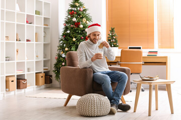 Young man in Santa hat with glass of milk and Christmas cookie at home