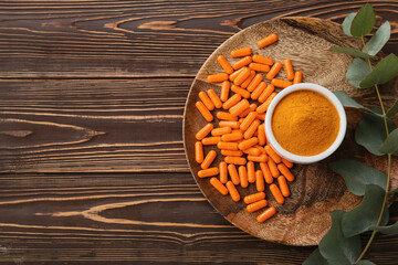 Bowl with turmeric powder and capsules on wooden background
