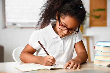 Naklejka na ściany i meble Little African-American girl writing in copybook while studying with online tutor at home