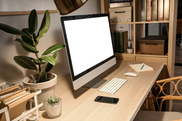 Workplace with modern computer, mobile phone and houseplant in dark room