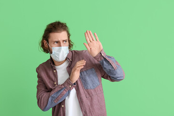 Scared young man wearing medical mask on color background