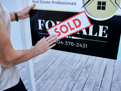 Another property sold. High angle shot of an unrecognizable female real estate agent sticking a sold sign over a for sale board.
