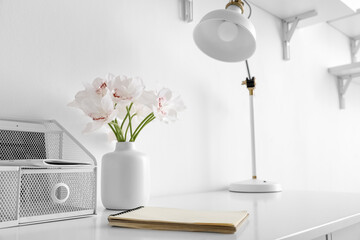 Comfortable workplace with beautiful flowers, organizer and notebook near white wall
