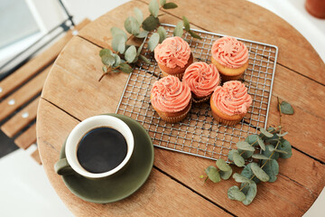 Neatly arranged and blog ready. High angle shot of freshly baked cupcakes on a metal tray and a cup of coffee on a table indoors.