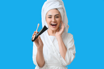 Beautiful young woman in bathrobe, with activated charcoal tooth paste and brush on blue background