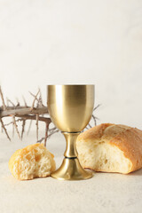 Cup of wine with bread and crown of thorns on light background