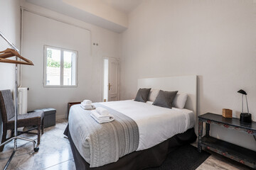 Bedroom with king size bed, wooden bedside table, stoneware floor, coat rack with wooden hangers,...