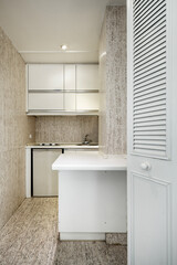 Small kitchen with white wooden furniture in a cubicle with marble walls and floors and Venetian-style white wooden doors