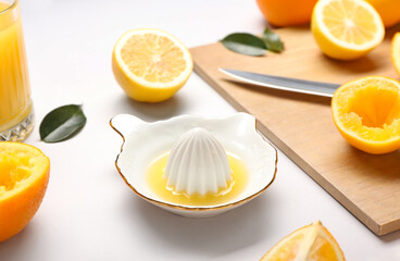Ceramic juicer, glass of juice, lemon and oranges on light background