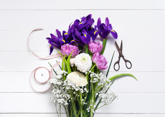 Bouquet of beautiful flowers, ribbon and scissors on light wooden background
