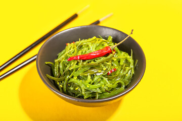 Bowl with healthy seaweed salad on yellow background