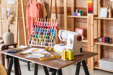 Tailor's workplace with sewing machine, thread spools and sketches in atelier