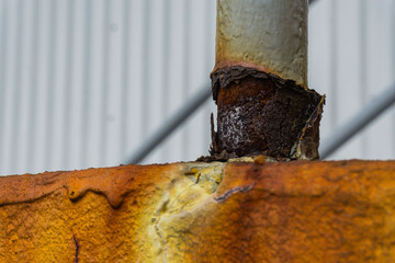 Decaying rusted pole at the base of safety railing on top of rust covered step.