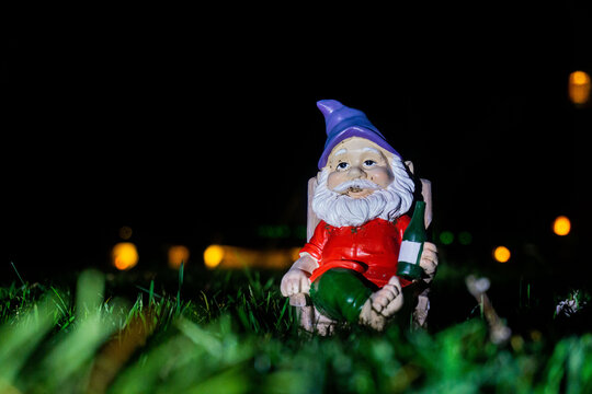 Garden gnome in front of black background relaxing on top of green grass in the middle of the night.