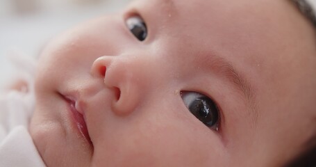 Close up macro portrait adorable newborn baby infant child girl face wakes up and opens his eyes looking at camera on the bed in the morning at home	
