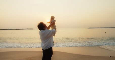happiness Asian family grandmother is keeping on her arms holding and playing with cute adorable newborn baby infant girl on a seaside beach at sunrise during holiday vacation in Thailand	
