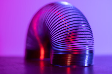 Closeup of coiled metal spring with sufficiently high strength and elastic properties in neon purple and pink light. Macro photo, selective focus.
