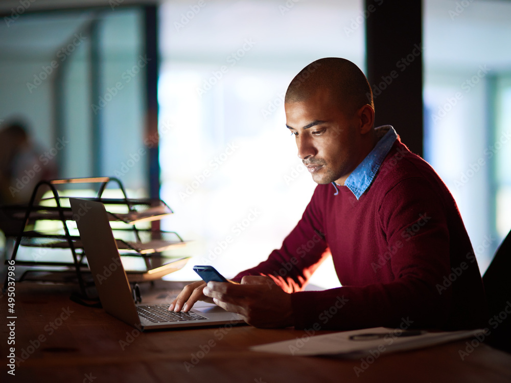 Poster Keeping in touch via text. Shot of a handsome young man sending a text while working late in his office.
