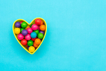 Chewing gum in the shape of colorful spheres forming a heart on a blue background.