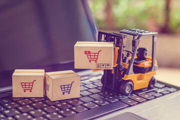 Logistics and supply chain management for online shopping concept : Fork-lift moves a box with a red shopping cart logo, 2 cartons on a laptop computer, depicts delivering goods or products in a store