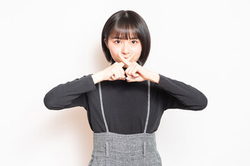 白い背景の前に立ってNGのポーズをする若い女の子