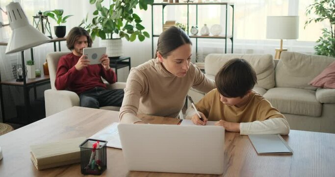 Mother helping son doing homework using laptop while father using digital tablet in the background