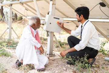 Engineer explaining to Indian farmer about sloar power generation operating below the panel module...