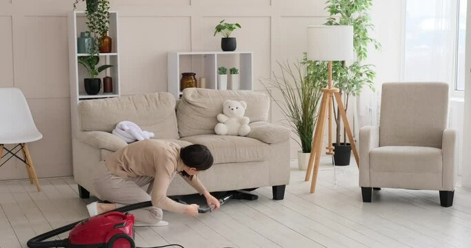Playful girl running towards her mother cleaning floor in the living room with vacuum cleaner