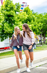 Two smiling teenage girls walking together at an outdoor carnival. Best friends having fun during summer vacation. Friendship and happiness.