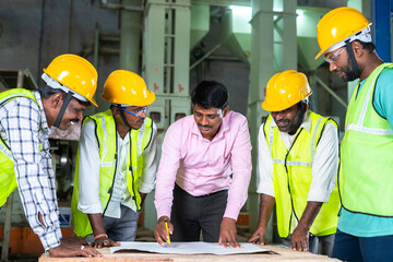 group of Industrial workers with planning engineer discussing about blueprint of construction at...
